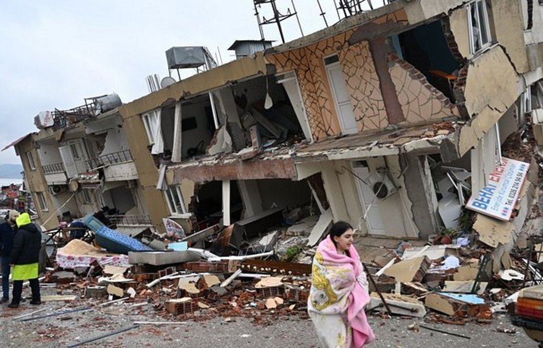 Eine Frau eilt, in eine Decke gehüllt, an einem zerstörten Wohngebäude vorbei