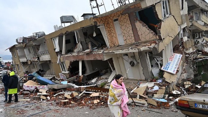 Eine Frau eilt, in eine Decke gehüllt, an einem zerstörten Wohngebäude vorbei